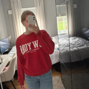 Röd sweatshirt med New York-tryck - Cool röd sweatshirt med stort vitt New York-tryck på bröstet. Tröjan har rund hals, långa ärmar och ribbade muddar vid ärmslut och nederkant. Perfekt för dig som gillar sportig och avslappnad stil.