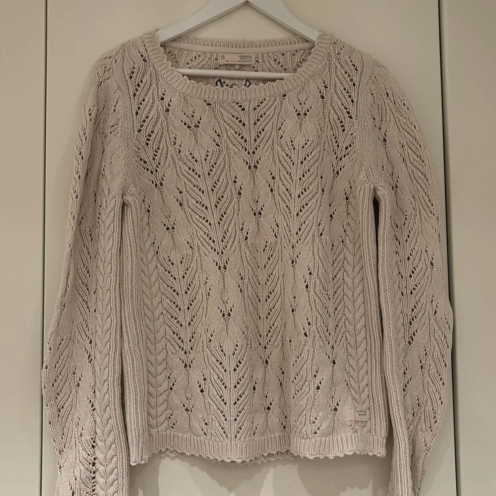 Supersnygg beige stickad tröja från Odd Molly med hålmönster och rund hals. Tröjan har långa ärmar och fina detaljer, inklusive broderad logga på ryggen. Perfekt för lager-på-lager och en mysig stil.. Neuleet.
