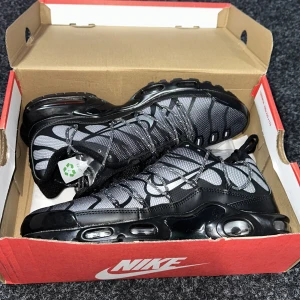 Nike Air Max sneakers i svart och grå - Säljer ett par Nike Air Max sneakers i svart och grå med vita detaljer. Skorna har snörning, synlig luftdämpning i sulan och en sportig design. 