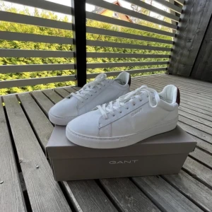 Vita sneakers från Gant - Säljer ett par stilrena vita sneakers från Gant med klassisk design. Skorna har rund tå, vita snören och diskret Gant-logga på sidan. Perfekta för dig som gillar en clean look och vill ha något som funkar till det mesta.