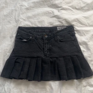 Svart jeanskjol med volang - Snygg svart jeanskjol från Zara med volangdetalj längst ner. Kjolen har en klassisk femficksdesign och stängs med knapp och dragkedja framtill. Perfekt för en trendig look!