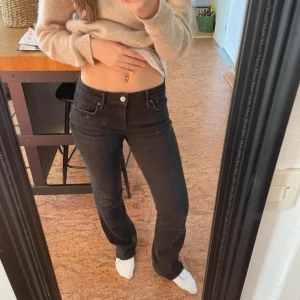 Svarta lågmidjade jeansbyxor - Säljer ett par svarta jeansbyxor med låg midja och klassisk femficksdesign. Byxorna är bootcut och stängs med dragkedja och knapp. Perfekta för en avslappnad och stilren look.