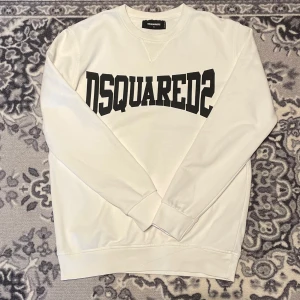 Vit sweatshirt från Dsquared2 - Säljer en vit sweatshirt från Dsquared2 med stor svart logga över bröstet. Tröjan har rund halsringning och långa ärmar. Klassisk och stilren design, perfekt för en avslappnad look. Två små fläckar se bild 2/3. Står S men passar XS bättre. Vid fler bilder skriv pm.