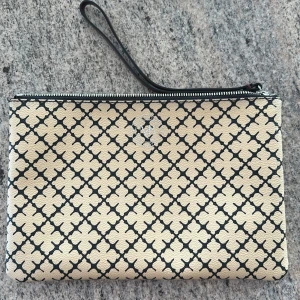 Beige och svart kuvertväska från By Malene Birger - Snygg kuvertväska från By Malene Birger i beige och svart med klassiskt grafiskt mönster. Väskan har dragkedja upptill och en handledsrem. Insidan är fodrad med flera fack för enkel organisering. Perfekt accessoar för att lyfta din outfit.