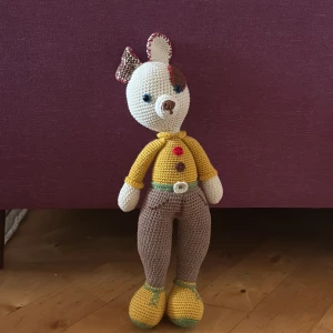 Handvirkad nalle i färgglada kläder - Säljer en handvirkad nalle med vit och brun kropp, gula skor, bruna byxor och gul tröja. Nallen har detaljer som färgglada knappar och ett litet bälte. Perfekt som present eller dekoration.