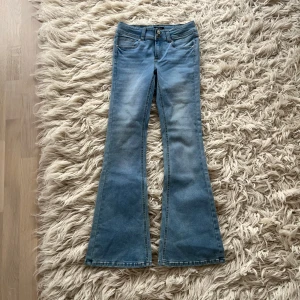 Nya low waist bootcut jeans från RYVLS - Säljer ett par helt nya ljusblå bootcut jeans stl 164 från RYVLS Stockholm med låg midja. Jeansen har klassisk femficksdesign med ficklock, dubbla knappar i midjan.  