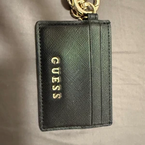 Svart korthållare från Guess - Plånbok från guess med 3 fack som är välanvänd. Tyget på ena facket är lite löst.