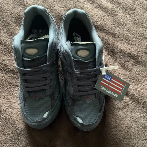 New Balance 2002 Protection Pack (Phantom) - Säljer ett par gråa New Balance sneakers med mesh och mockadetaljer. Skorna har snörning och klassisk N-logga på sidan. Tillverkade i USA och kommer med originaltagg kvar. Perfekta för dig som gillar stilrena och bekväma sneakers. Skolådan medföljer! Nypris: 4599 kr