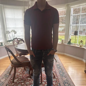 Vinröd pikétröja från Tiger of Sweden - Säljer en vinröd pikétröja från Tiger of Sweden med klassisk krage och korta ärmar. Tröjan har en diskret broderad logga på bröstet och är tillverkad i bomull. Perfekt för en stilren och avslappnad look. Mycket bra skick köpt för ca ett år sedan på NK för 1,3