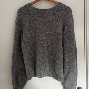 Grå stickad tröja - Mysig grå stickad tröja med rund halsringning och långa ärmar. Perfekt för kyliga dagar och enkel att matcha med olika outfits. Tröjan har en klassisk och avslappnad passform.