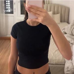 Svart ribbad croppad t-shirt - Säljer en svart croppad t-shirt med tight passform. Perfekt för en stilren och enkel look. T-shirten är kortärmad och gjord i ett mjukt material.