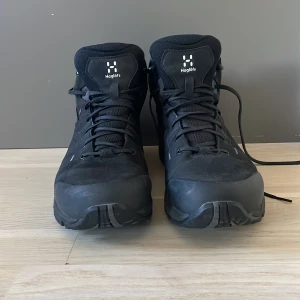 Svarta kängor från Haglöfs - Säljer ett par robusta svarta kängor från Haglöfs. De har snörning och en slitstark sula som ger bra grepp. Perfekta för utomhusaktiviteter och vandring. Kängorna är designade för att klara tuffa förhållanden och hålla fötterna torra och bekväma.