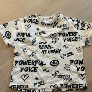 Vit t-shirt med svart textprint från Zara - Cool vit t-shirt från Zara med svart textprint och olika motiv som hjärtan, stjärnor och blixtar. T-shirten har rund hals och korta ärmar. Perfekt för dig som gillar statement-plagg med attityd! Passar barn och är i storlek 134