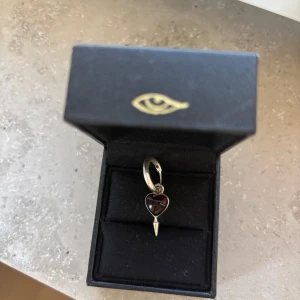 Maria Nilsdotter single love earring - Säljer ett snyggt örhänge från Maria Nilsdotter. I silver med ett rött hjärta och nit nertill. Just den här säljs inte längre och är verkligen så coolt, tappade tyvärr mitt andra😔😔❤️❤️