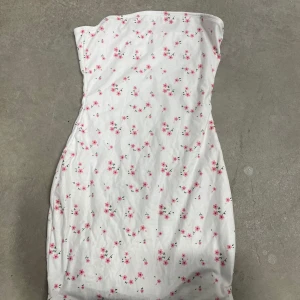 Vit blommig axelbandslös klänning från SHEIN - Supersöt axelbandslös klänning från SHEIN i vit med små rosa blommor. Klänningen har en tight passform och är i mjuk polyesterblandning. Perfekt för sommarens alla tillfällen!