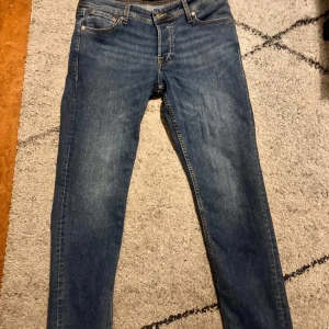 Blå jeansbyxor med klassisk passform - Säljer ett par blå jeansbyxor med normal passform och raka ben. Byxorna har fem fickor, dragkedja och knapp framtill samt klassiska sömmar på bakfickorna. Perfekta till vardags och enkla att matcha med olika stilar. Använt 1 gång storlek 30/30