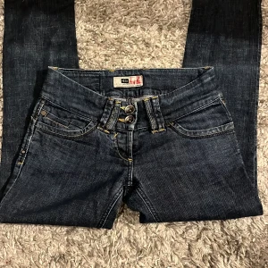 Mörkblå jeansbyxor med dubbla knappar - Säljer ett par mörkblå jeansbyxor från river island med dubbla knappar i midjan och dekorativa bakfickor med lock och knappar. Jeansen är lågmidjade och raka. Står #8/34 i jeansen men skulle säga xs. Innebenslängd: 69cm midja: 37cm 