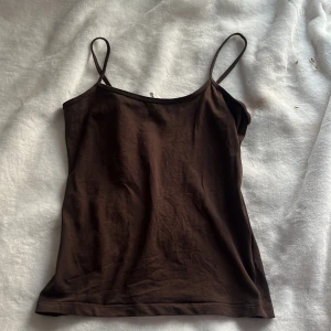 Brun linnetopp från Åhléns Woman - Säljer en brun linnetopp från Åhléns Woman i storlek S. Toppen har smala axelband och är tillverkad i mjuk bomull, perfekt för varma dagar eller som layering-plagg.