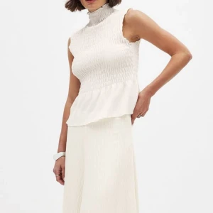 Vit ärmlös klänning - Elegant vit topp med hög krage och smockdetaljer. Den är ärmlös och är Perfekt för sommarens alla tillfällen.