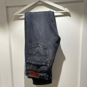 Levis 501 nypris 1200 kr - Snygga svarta jeans från Levi's med klassisk femficksdesign och knappgylf. Perfekta för en stilren look. Levi's-logga på bakfickan och läderpatch vid midjan.