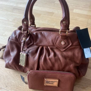 Marc by Marc Jacobs classic Q Leather bag - Säljer en snygg brun trendig marc by marc Jacobs skinnväska med matchande plånbok. Väskan har både handtag och axelrem samt en dragkedja upptill.  Oanvänd. 