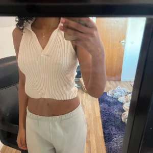 Vit ribbad croppad linnetopp med krage - Säljer en vit ribbad croppad linnetopp med bred krage och v-ringning. Toppen är ärmlös och har en tight passform, perfekt för en trendig och stilren look.