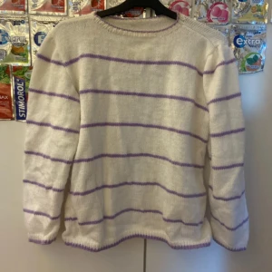 Vit stickad tröja med lila ränder - Supermysig stickad tröja i vitt med lila horisontella ränder. Tröjan har rund halsringning med lila kant och långa ärmar. Perfekt för lager-på-lager och chill dagar. Passar dig som gillar en enkel men ändå söt stil.