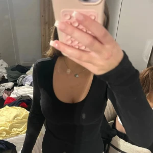 Svart ribbad långärmad tröja - Snygg svart långärmad tröja med djupare rundad ringning. Tröjan är ribbad och sitter tight, perfekt att styla med jeans eller kjol. Enkel och stilren design som passar till många olika looks.