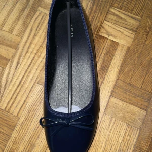 Mörkblå ballerinaskor med rosett - Snygga mörkblå ballerinaskor från Nelly med glansig finish och söt rosettdetalj framtill. Skorna har rund tå och platt sula, perfekta för en clean och stilren look. Tillverkade i syntetmaterial som ger en modern vibe.