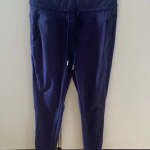 Mörkblå träningsbyxor med snörning S - Mörkblå träningsbyxor i sportig stil med dragsko i midjan och smal passform. Byxorna är tillverkade i ett stretchigt material med 77% nylon och 23% elastan, vilket gör dem perfekta för träning eller chill. Snygga sömdetaljer och bekväma fickor på sidorna.