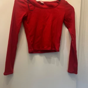 Röd croppad långärmad topp - Snygg röd croppad topp med långa ärmar och rundad halsringning. Enkel och stilren design som passar perfekt till jeans eller kjol. Toppens material känns mjukt och följsamt mot kroppen och den har en tight passform som framhäver figuren.