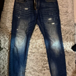 Blå jeans från Alessandro Zavetti - Snygga blå jeans från Alessandro Zavetti med slitna detaljer och coola färgstänk. Jeansen har en markerad dragkedja framtill, klassisk femficksdesign och smal passform. Perfekta för dig som gillar en streetinspirerad look.