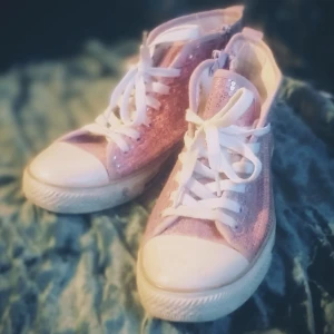 Rosa glittriga sneakers med paljetter - Snygga rosa sneakers med vita snören och tå, dekorerade med glittriga paljetter för extra bling. Skorna har en klassisk rund tå och platt sula, perfekt för dig som vill sticka ut med en färgglad och lekfull stil.