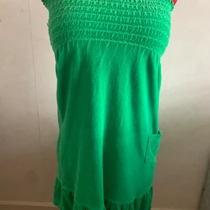Grön tubklänning Juicy Couture - Snygg grön tubklänning från Juicy Couture i mjuk frotté. Klänningen är kort, har smock upptill, liten ficka på sidan och volangkant nertill. Perfekt för sommarens chill dagar eller när du vill ha något bekvämt men ändå cute.