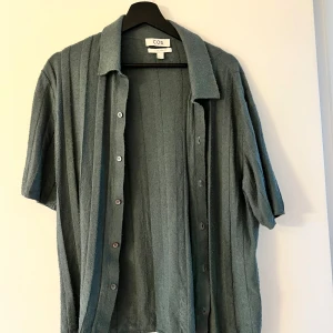 Grå ribbad skjorta från COS - Säljer en grå skjorta från COS i relaxed fit med kort ärm och knappar framtill. Skjortan har ett ribbat mönster och är tillverkad i ett mjukt, texturerat material som ger en chill och modern vibe. Perfekt för dig som gillar en loose och avslappnad stil.