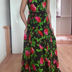 Summer floral långklänning från ASOS - Supersnygg långklänning från ASOS med svart botten och stora blommor i rött och rosa samt gröna blad. Omlottmodell med v-ringning och knyt i midjan. Perfekt för dig som vill sticka ut med färg och mönster. Luftigt material och flowig passform.