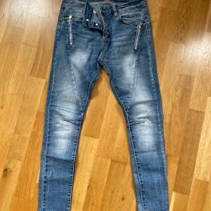 Blå skinny jeans från Lexxury - Snygga blå skinny jeans från Lexxury med slitningar och coola dragkedjor framtill. Jeansen har en stjärndetalj på bakfickan och en tvättad look som ger en avslappnad vibe. Perfekta för dig som gillar en smal passform och streetstyle.