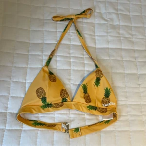 Gul bikiniöverdel med ananasmönster - Snygg gul bikiniöverdel från Blancheporte med ananasmönster. Triangelformade kupor och knyt i nacken ger en snygg och cool strandlook. Perfekt för sommarens alla bad och poolhäng.