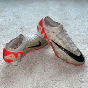 Nike Mercurial Vapor 15 Zoom fotbollsskor - Hej säljer mina NIKE AIR ZOOM MERCURIAL VAPOR 15 ELITE FG READY - RÖD/VIT/SVART fotbollsskor. Ovandelen är i syntetmaterial med snörning och låg profil. Sulan har röda dobbar för bra grepp på planen. Perfekta för dig som vill ha snabba och lätta skor till matchen. Fråga om du vill ha fler bilder eller har andra funderingar   MVH Axel 🤝