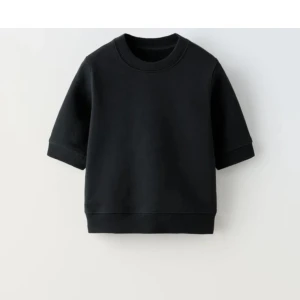 Svart stickad tröja från Zara - En svart stickad tröja från Zara med korta ärmar och rund halsringning. Tröjan har en enkel och clean design med ribbade muddar vid ärmslut och nederkant. Perfekt för dig som gillar en stilren och basic look.