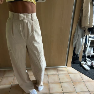 Beiga vida kostymbyxor H&M strl 34 - Säljer ett par beiga kostymbyxor från H&M i storlek 34. Byxorna är högmidjade med vida ben 