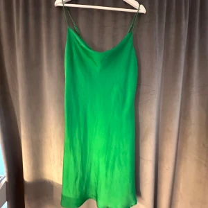 Grön ärmlös kortklänning - Snygg grön kortklänning med tunna axelband och enkel, rak passform. Klänningen har en slät yta och är perfekt för dig som gillar minimalistisk stil. Den är ärmlös och har en fräsch, klar grön färg som verkligen sticker ut.
