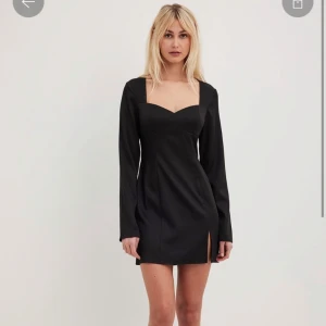 Svart kort klänning från NA-KD - Supersnygg svart kort klänning från NA-KD med långa ärmar, fyrkantig urringning och en liten slits framtill. Figurnära passform som framhäver midjan. Perfekt för dig som vill ha en stilren och trendig look. Endast använd 1 gång för 2-3 år sedan. 