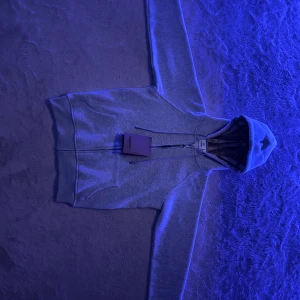 Grå hoodie från Burberry med dragkedja - Snygg grå hoodie från Burberry med klassiskt rutigt foder i huvan och broderad logga på bröstet. Tröjan har hel dragkedja, snörning i huvan och stora fickor framtill. Perfekt för dig som vill ha en stilren och lyxig look. Det står S fast känns som XS, hade två Burrberry hoodies👍