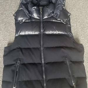 Svart dunväst från Polo Ralph Lauren - Dunväst från Polo Ralph Lauren som är svår att hitta. 7/10 i skick. Går inte att spänna i midjan eftersom bandet har gått sönder. Nypris: runt 5000