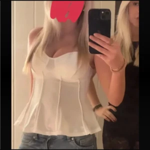 Vit korsett-topp med markerade sömmar - Snygg vit korsett-topp med markerade sömmar och utsvängd nederdel. Toppen har en figurnära passform upptill och är ärmlös med breda axelband. Perfekt att styla med jeans eller kjol för en trendig look.