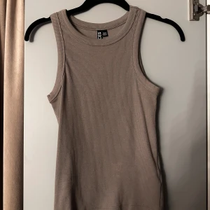 Beige ribbad linnetopp från Pieces - Säljer en stilren beige ribbad linnetopp från Pieces. Toppen är ärmlös med rund halsringning och har en tight passform som sitter snyggt på kroppen. Perfekt att matcha med jeans eller kjol för en clean look.