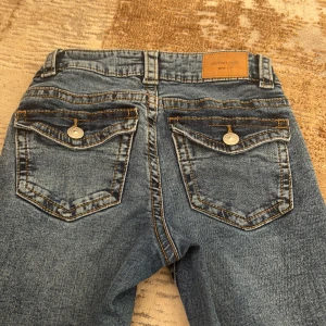 Blå bootcut jeans från Gina Tricot - Säljer ett par klassiska blå bootcut jeans från Gina Tricot, modell Perfect Jeans. Jeansen har snygga bakfickor med lock och knapp, samt kontrastsömmar. Storlek 32