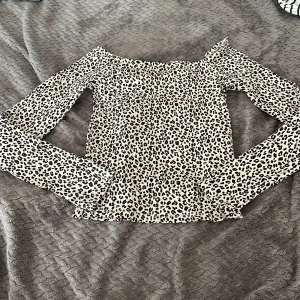 Leopardmönstrad offshoulder topp Gina Tricot - Snygg offshoulder topp från Gina Tricot i leopardmönster. Toppen är vit med svarta och beige fläckar, har långa ärmar och sitter tight. Perfekt för dig som vill sticka ut med ett trendigt djurmönster. Köpt för jätte länge sen från Gina, använd 3 gr kanske.❤️