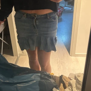 Jeanskjol med volangkant - Snygg ljusblå jeanskjol med volang nertill och klassiska fickor fram och bak. Kjolen har en feminin touch med den vågiga volangkanten och stängs med knapp och dragkedja framtill. Perfekt för dig som gillar denim och vill ha en cool men söt look. Kjolen har jag sytt själv och blev inte helt nöjd, den har vissa defekter som att några stygn i ena sidan syns, därför säljer jag den lite billigare. Storlek w27.Den är för liten för mig och därför sitter den lite tajt på mig. 